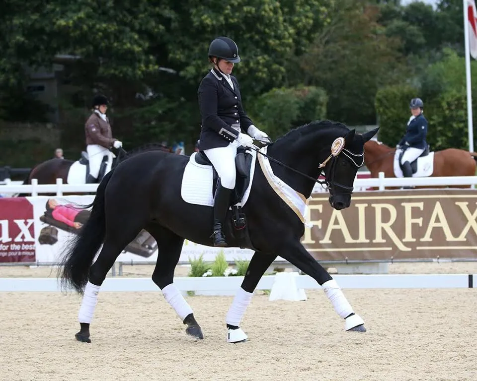 Amanda riding a black horse with a rosette at an international para dressage show