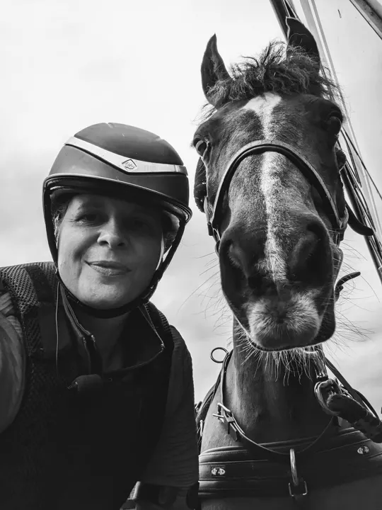 Black and white selfie of Amanda in her riding hat beside Ranger