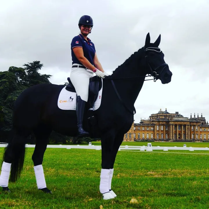 Amanda in GB polo shirt on a black horse with Blenheim Palace behind