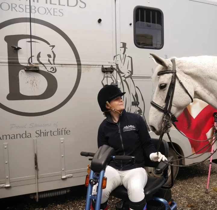 Amanda on her mobility scooter beside her grey mare Ruby Rose II and a Bloomfields horsebox lettered Proud Sponsors of Amanda Shirtcliffe
