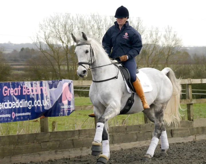 Amanda riding a grey horse in an outdoor arena