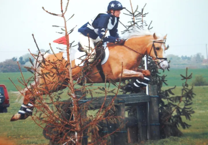 Amanda jumping a brush fence cross-country on her palomino, Miden Moondancer