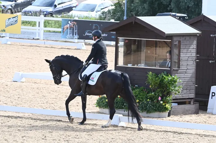 Amanda riding a black horse past a judge’s box at an outdoor dressage show