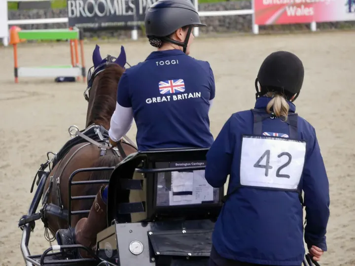 Amanda from behind in a Great Britain team shirt on her carriage, with her groom wearing number 42