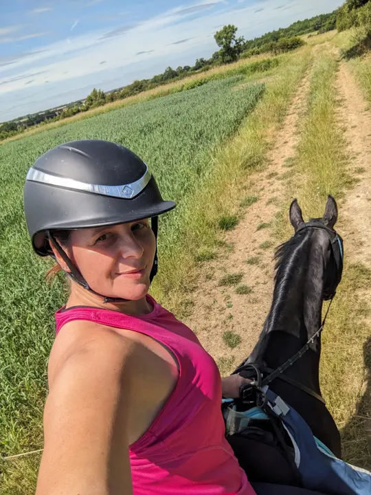Amanda in a pink top taking a selfie on horseback beside a field