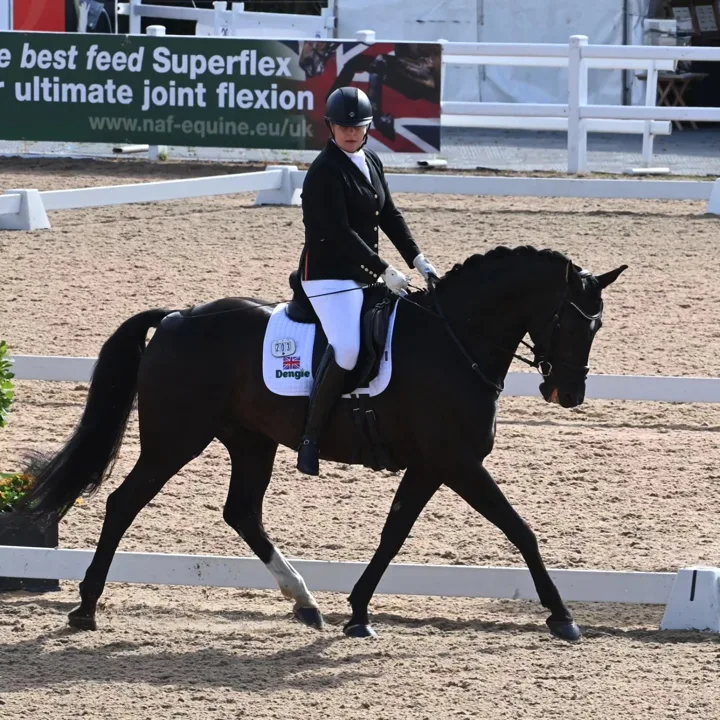 Amanda riding Hermione in extended trot at Hartpury beside a sponsor banner