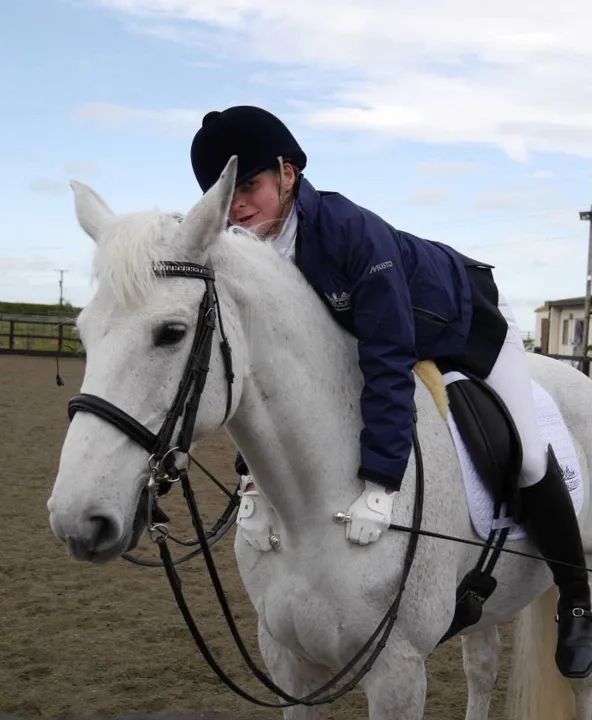 Amanda leaning forward to hug the neck of her grey mare Ruby Rose II