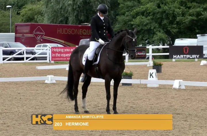 Amanda riding Hermione in an outdoor arena, with an on-screen caption showing their names