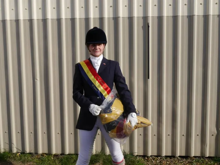 Amanda in show jacket wearing a red, yellow and blue winner’s sash and holding a rosette