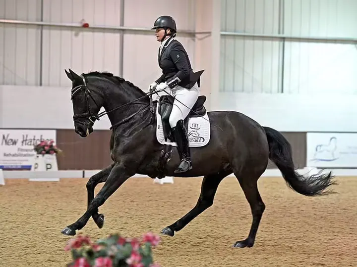 Amanda riding a black horse in canter in an indoor dressage arena
