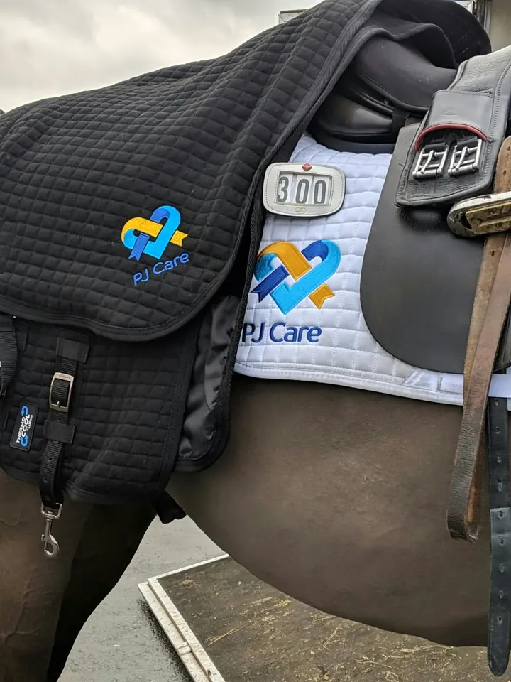 A black PJ Care cooler rug and a white PJ Care saddle pad on Amanda’s horse at a show