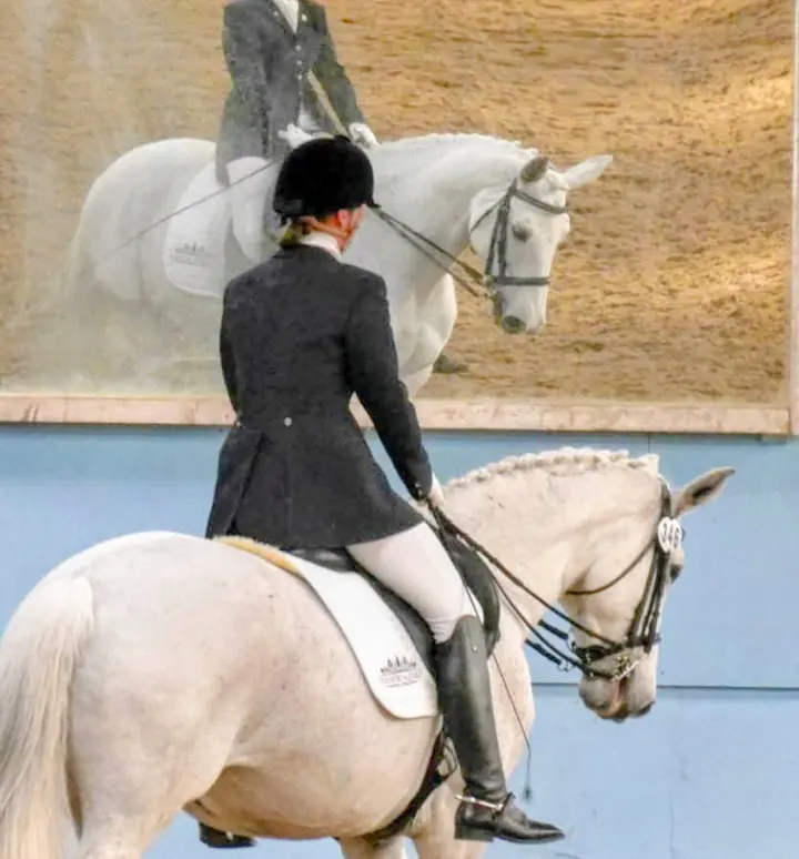 Amanda riding the grey mare Run of the Mill in an indoor arena