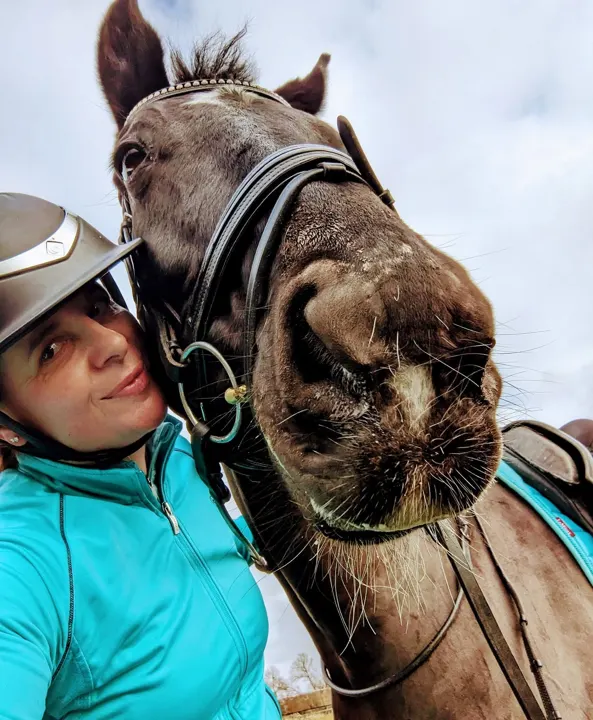 Amanda in a turquoise jacket taking a selfie with a bay horse