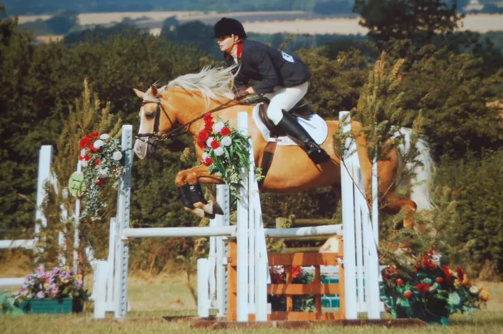 A young Amanda show jumping her palomino, Miden Moondancer, over a fence decorated with flowers