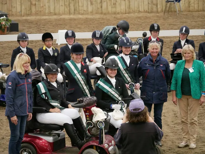 Amanda on her mobility scooter with team-mates in green sashes at a prize-giving in an indoor arena