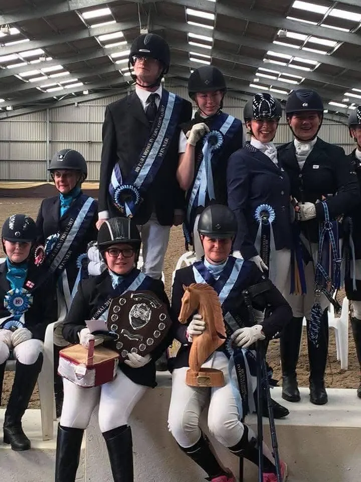 Amanda with team-mates holding a shield and trophies, wearing champions’ sashes and rosettes