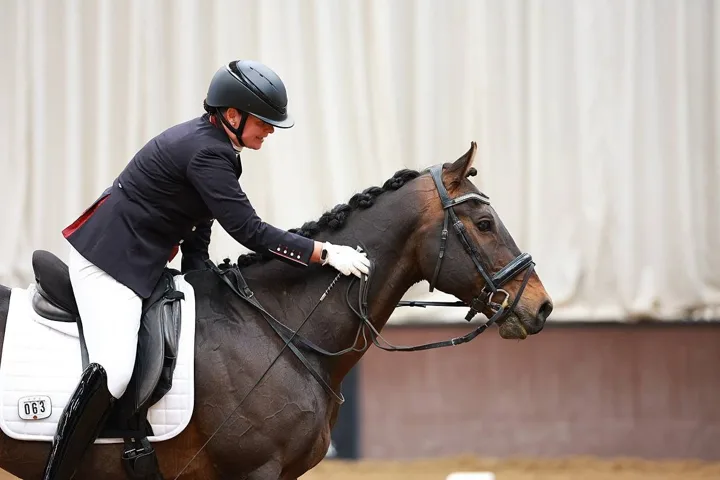 Amanda patting her bay horse Kirkstall Spirit’s neck in an indoor arena